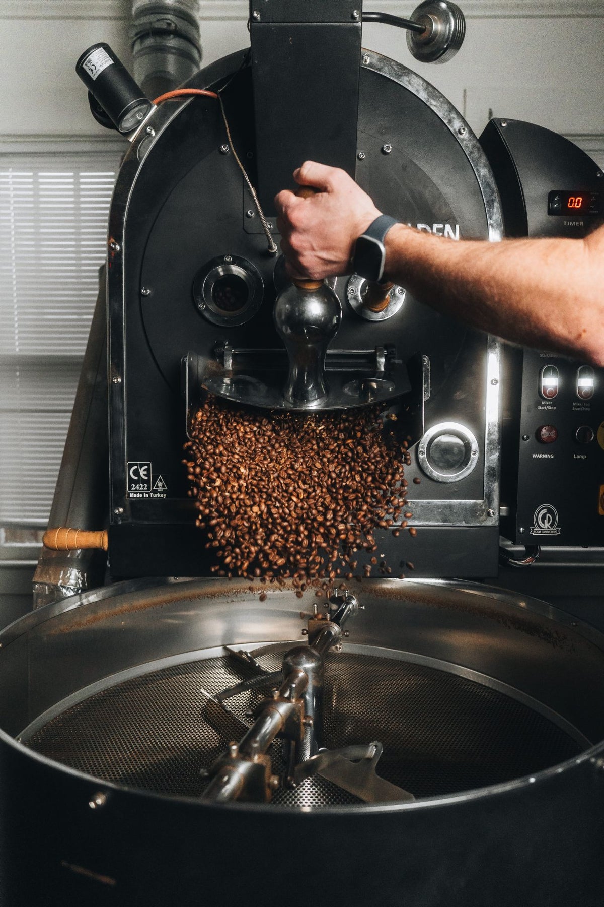 Roaster pouring freshly roasted coffee beans into the cooling tray at Village Coffee